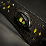 Macro of the Night Dragon Collar: green dragon eye with slit pupil under layered black leather eyelids, crocodile-embossed leather, yellow diamond inlays, green crystals and silver studs