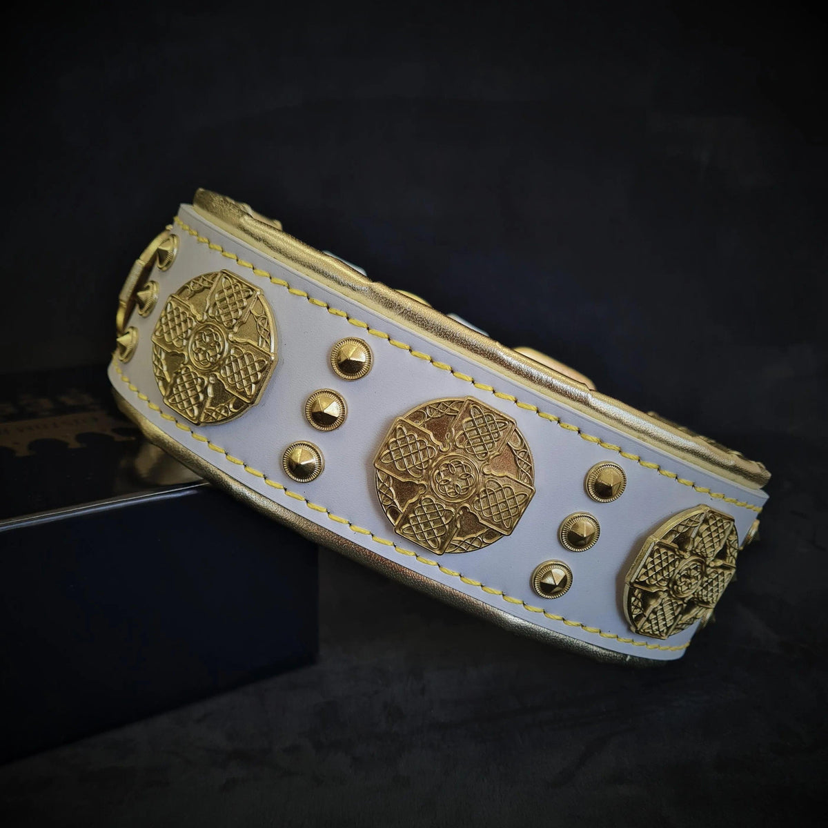 Close-up of the “Maximus” collar: white leather with gold-tone medallions and rivets